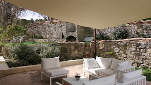 Un patio con mobiliario blanco, un muro de piedra y una chimenea de piedra.