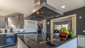 A modern kitchen with a central island, stainless steel appliances, and a large window providing natural light. - Es Garrover Es Velar with XXL pool, playground, volleyball, billiards, gym.. (Muro)