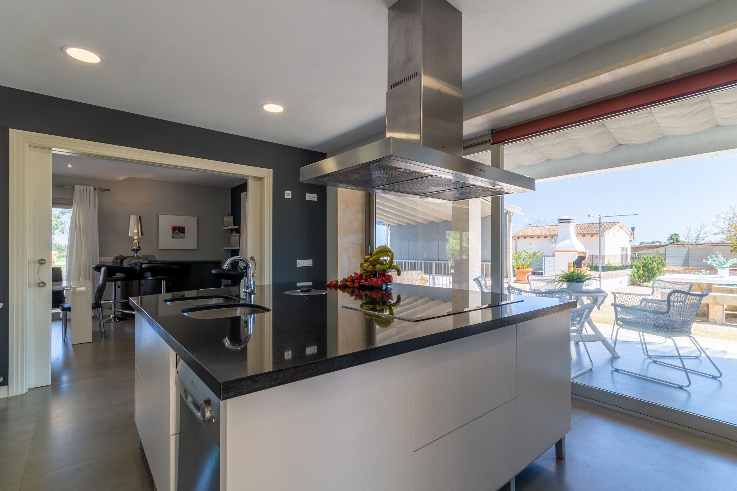 Une cuisine moderne dotée d’un îlot central, d’une hotte en acier inoxydable et offrant une vue sur la terrasse extérieure.