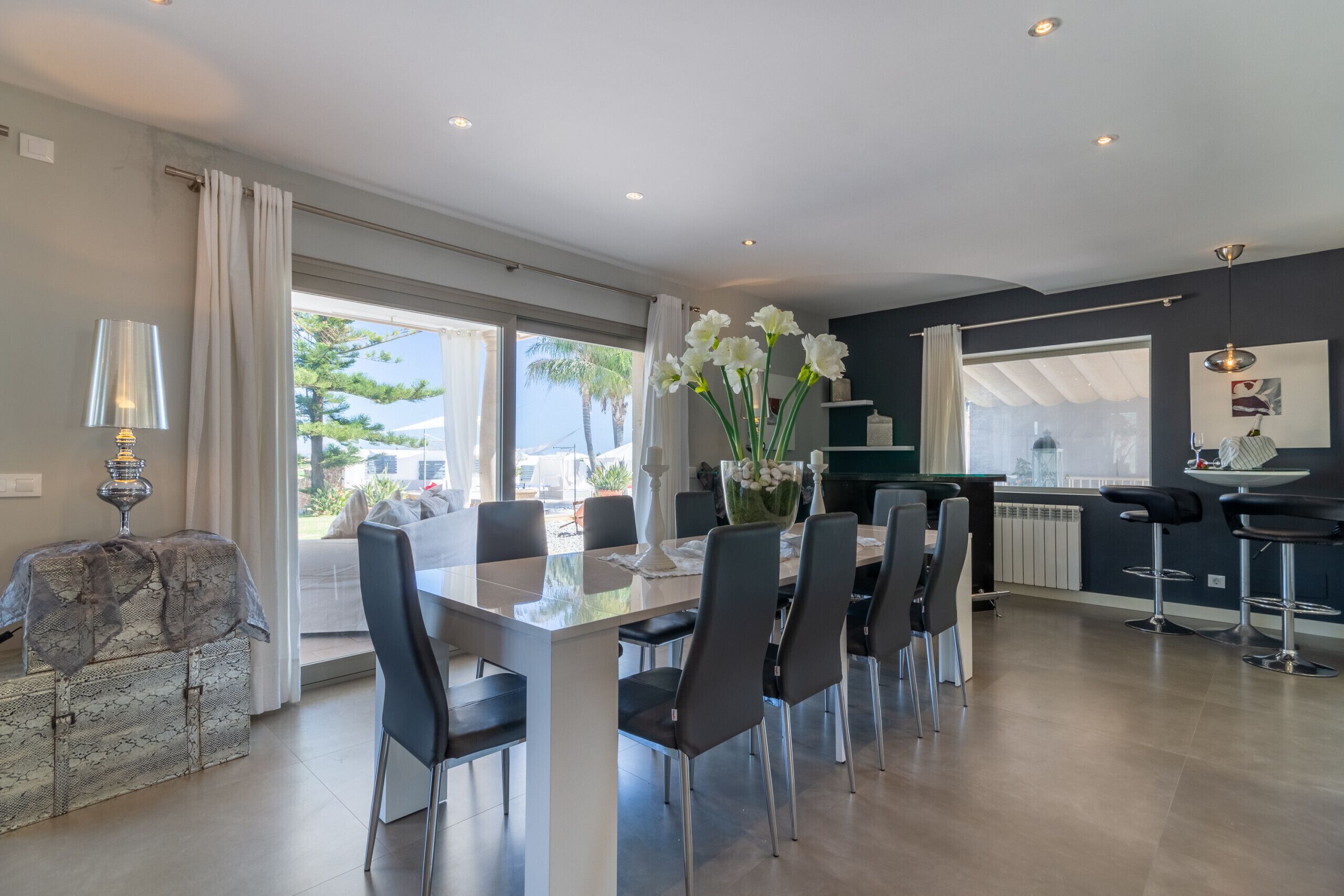 A modern dining area with a glass-top table, black chairs, and a vase of white flowers.