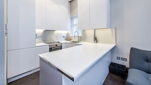 A modern kitchen with white cabinetry, a central island, and a built-in oven. - The One Paddington (London)