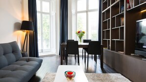 A modern living room with a sofa, a coffee table, a dining table with chairs, a bookshelf, and a TV. - The One Paddington (London)