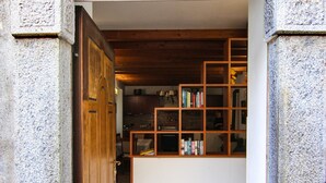 Un portail en arc donne accès à une pièce dont le sol est recouvert de carreaux et qui est équipée d’une bibliothèque en bois.