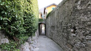 Un étroit sentier de pierres, bordé d’une végétation luxuriante et d’un mur de pierres, mène à un bâtiment dont l’entrée est bien visible.
