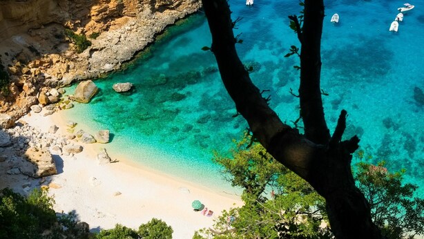 Un paisaje costero con aguas turquesas cristalinas, acantilados rocosos y una playa de arena.