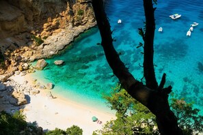 A coastal landscape with clear turquoise waters, rocky cliffs, and a sandy beach.