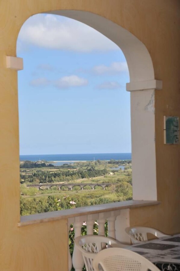 A balcony with a view of a coastal landscape, including a bridge and greenery.