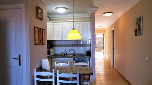 Una cocina con armarios blancos, encimera de granito, lámpara colgante amarilla y un comedor con mesa y sillas blancas.