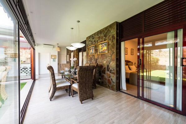 A modern dining area with wicker chairs, a glass table, and a stone accent wall.