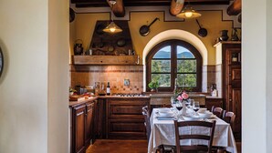 Una cocina rústica con armarios de madera, una estufa a gas y un comedor con mesa preparada para cuatro comensales.