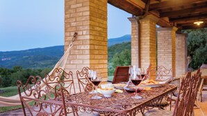Un área de comedor al aire libre con una mesa lista para dos personas, con sillas de metal y vistas al campo.