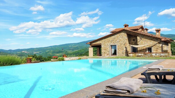 Una villa de piedra con piscina, rodeada de exuberante vegetación y montañas.