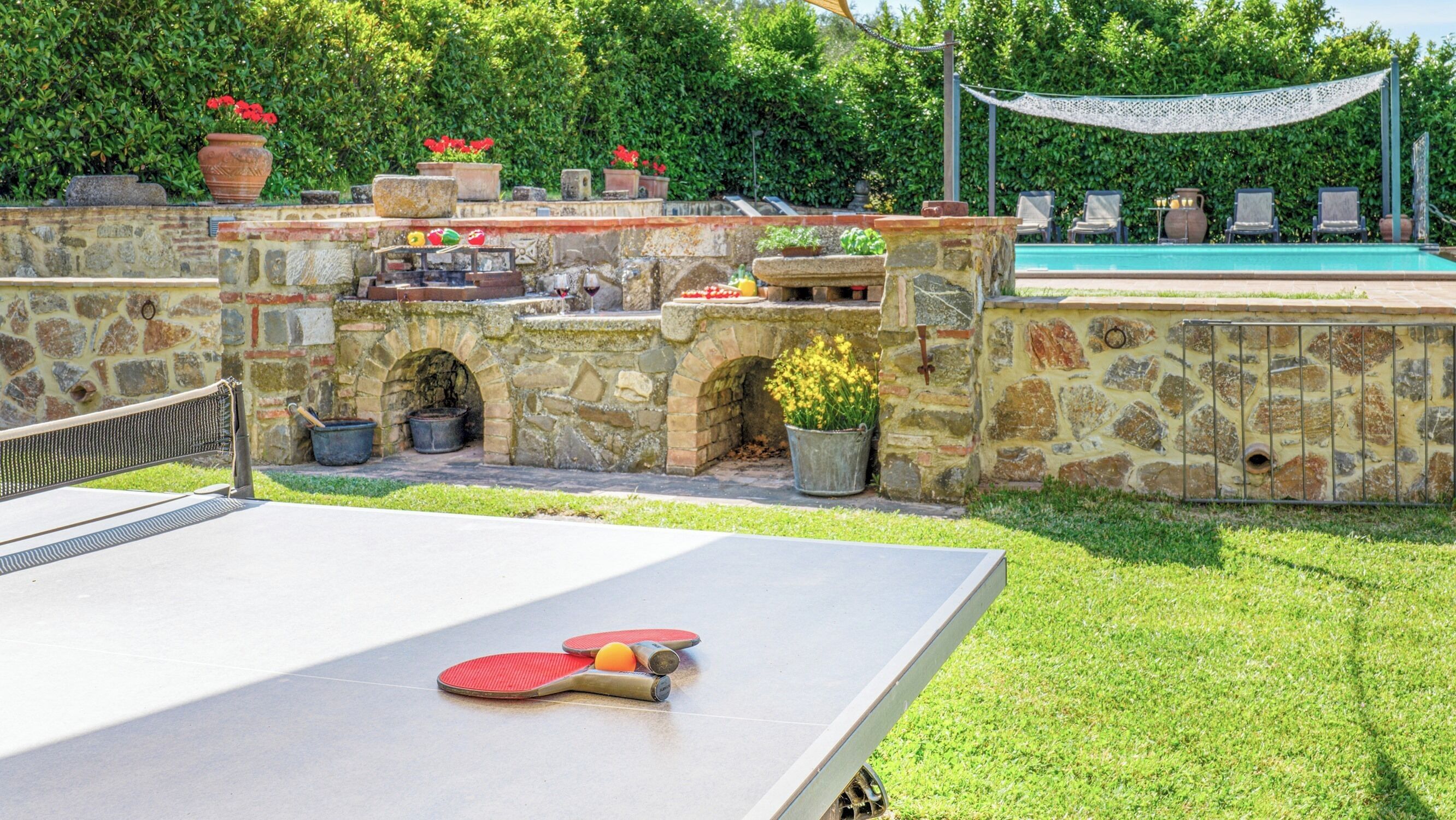 An outdoor pool area with stone walls, a ping pong table, and a hammock.