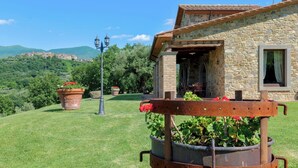 Una casa de piedra con una entrada rústica, un césped con plantas en macetas y vistas a colinas distantes.