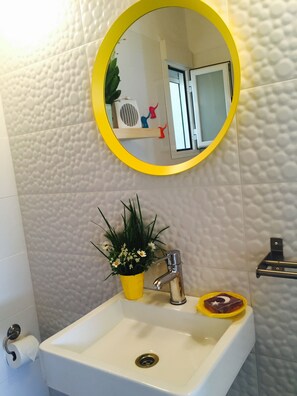 Een badkamer met een wit wastafelmeubel, een gele spiegel en een kamerplant.