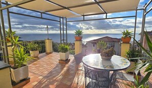 Une terrasse couverte avec une table et des chaises, des plantes en pot et une vue sur la mer.