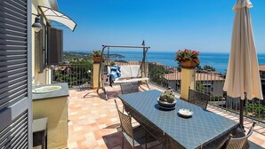 Eine Terrasse mit Tisch, Stühlen, einer Hängematte, einem Blumentopf und Blick aufs Meer.