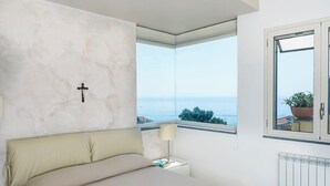 Ein Schlafzimmer mit Bett, Nachttisch mit Lampe, Fenster mit Meerblick und Heizkörper.
