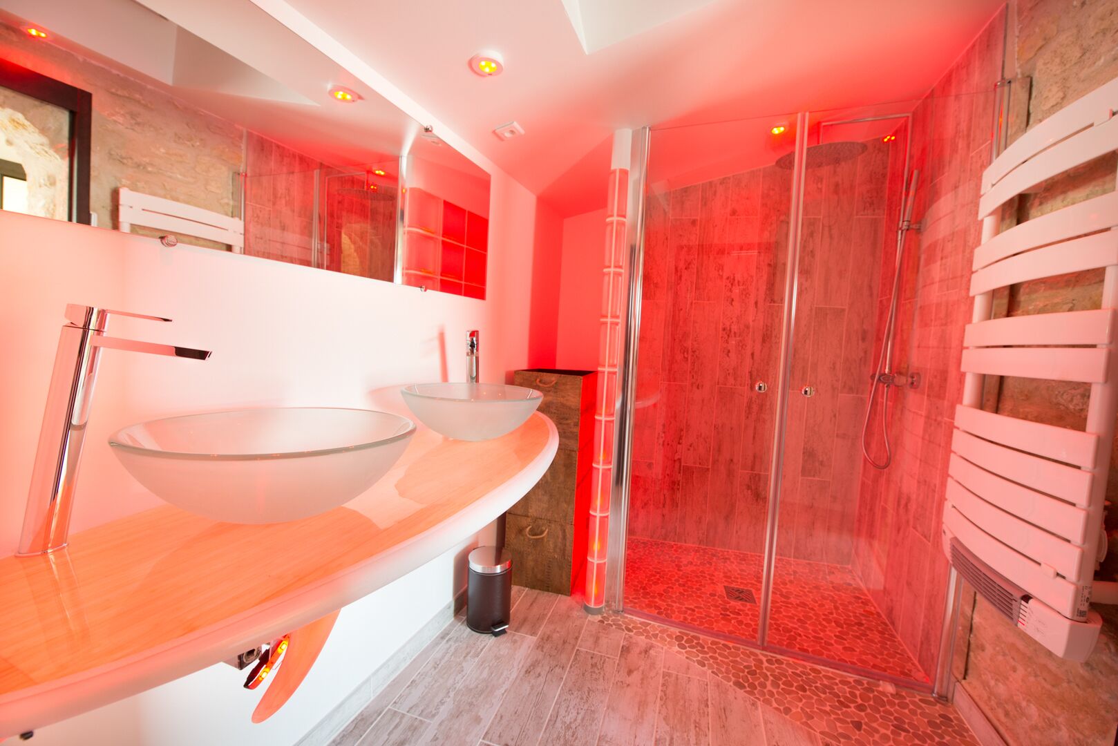 A modern bathroom with two glass sinks, a walk-in shower, and a wooden vanity.