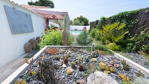 A garden with various cacti and succulents, a pool, and a white building with a red roof. - Holiday home, Ile d'Oléron 'L'Eglade' 4 star rating * * * * (Le Grand-Village-Plage)