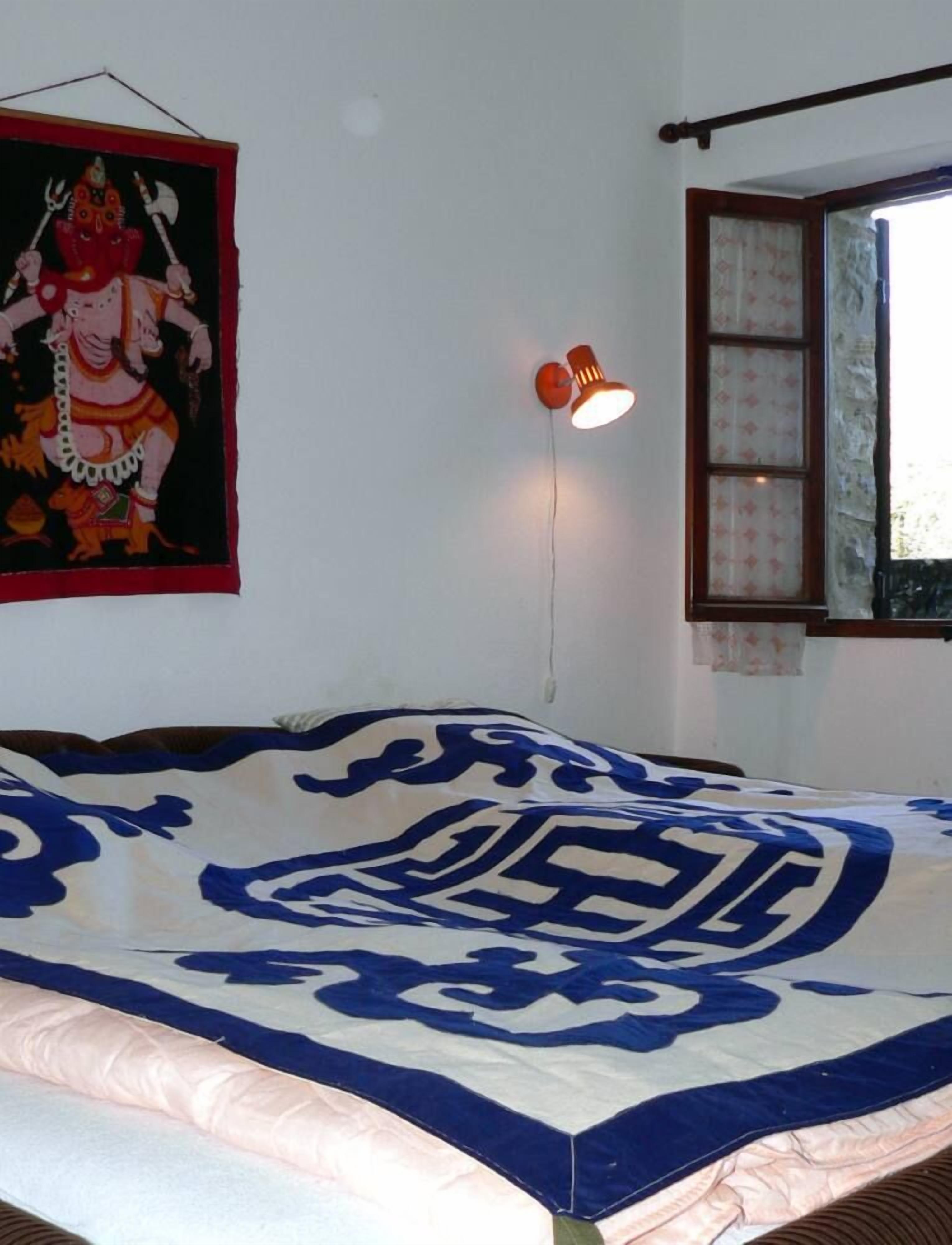 A bedroom with a bed, a wall hanging, a window, and a wall-mounted lamp.