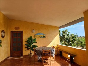 Eine Terrasse mit Tisch und Stühlen, einem Blumentopf, einer Tür und einem an der Wand befestigten Schild.