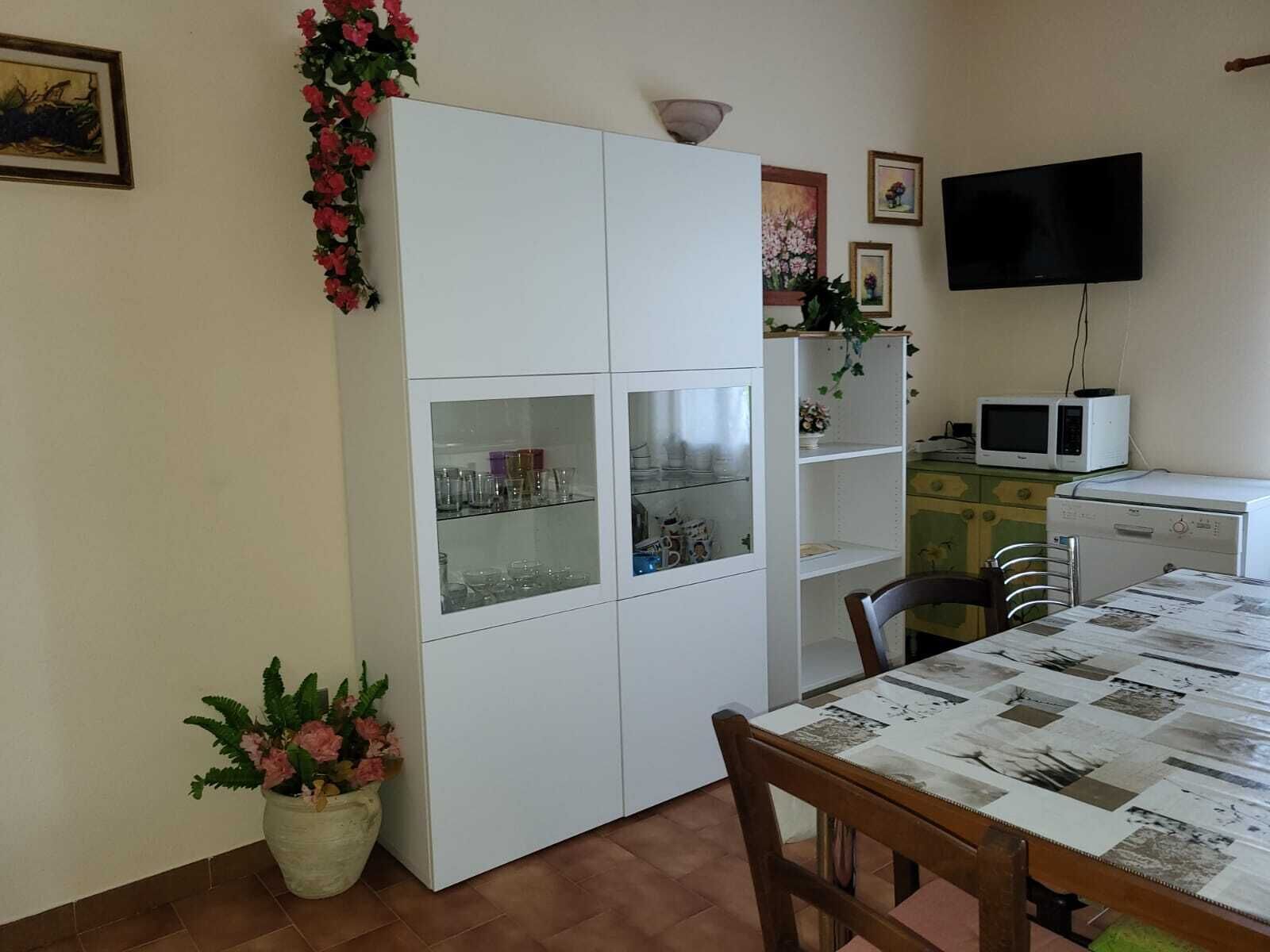 Un coin repas avec un meuble blanc, une table sur laquelle est posé un journal et un téléviseur fixé au mur.