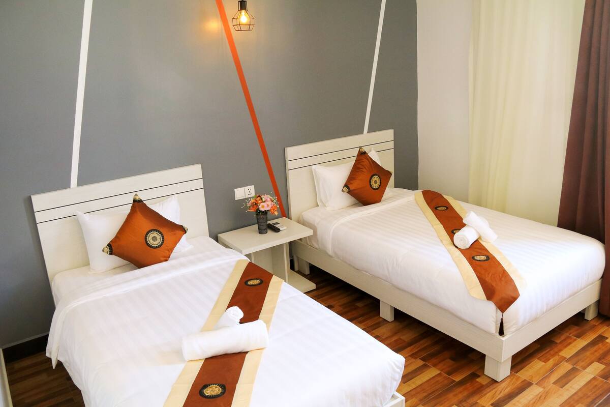 Dos camas juntas con cabeceros blancos, almohadas decorativas marrones y una toalla marrón sobre cada una.