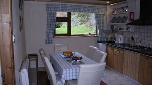 Een keuken met een eettafel, stoelen, een raam met gordijnen en uitzicht op de tuin.