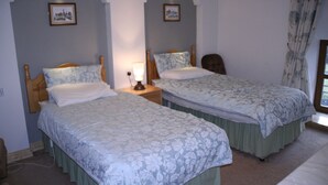Een slaapkamer met twee eenpersoonsbedden, elk met een houten hoofdbord, een nachtkastje met een lamp en een fotolijst aan de muur.