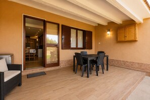 Eine Terrasse im Freien mit Tisch und Stühlen, einer Couch und einer Glastür, die in einen Innenbereich führt.
