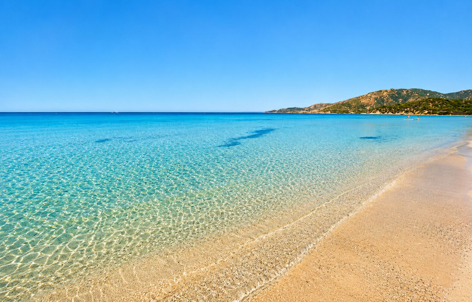 A beach with clear shallow waters and a sandy shore.