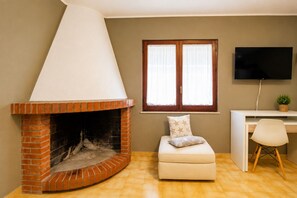 A living room with a brick fireplace, a white sofa, a desk with a computer, and a TV mounted on the wall.