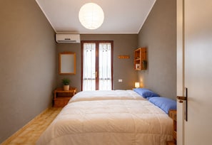 Un dormitorio con dos camas, una mesita de noche con lámpara, un espejo y una repisa con una planta.
