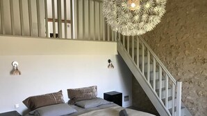 Een slaapkamer met een bed, nachtkastje, een wandlamp, een trap en een structuurmuur.