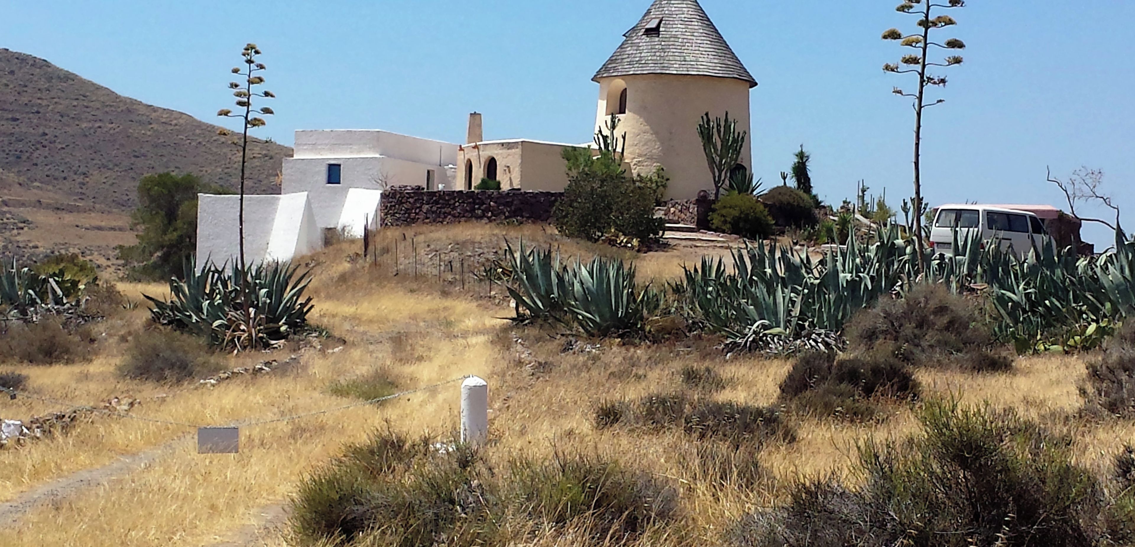 Un bâtiment doté d’un toit conique et d’une façade blanche, entouré de plantes d’agave et d’un paysage aride.