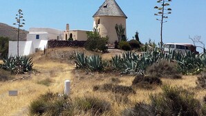 Un edifici amb un teulat cònic i façana blanca, envoltat de plantes d'aloca i un paisatge sec.