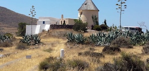 A building with a conical roof and a white exterior, surrounded by agave plants and a dry landscape. - Mojacar - Character villa 2 large bedrooms. Breathtaking view. (Mojacar)