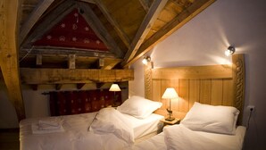 A cozy room with two beds, wooden beams, a red patterned wall, and two bedside lamps.