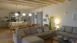 Un salon moderne avec un canapé d’angle, un coin repas avec une table et des chaises en bois, et une cuisine en arrière-plan.