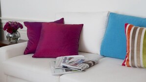 Un divano bianco con tre cuscini dai colori diversi e un tavolino laterale con un vaso di fiori.