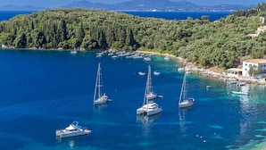A coastal area with several sailboats anchored near a small island with dense trees.