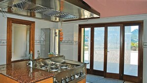 A kitchen with a gas stove, a stainless steel range hood, and a large window overlooking a balcony.