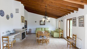 A spacious living area with a wooden ceiling, a fireplace, and a dining table surrounded by chairs.