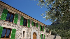 A stone building with green shutters, a wooden door, and a staircase leading to a higher level.