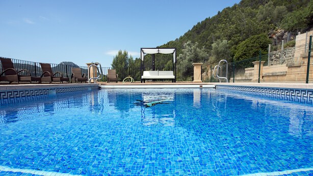 A clear blue pool with a tiled edge, a canopy, and a view of a mountainous landscape.