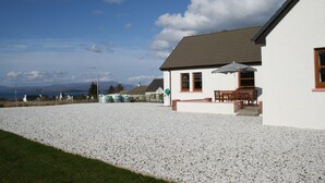 Una casa con vialetto in ghiaia, un patio con mobili da esterno e vista sul mare e sulle montagne.