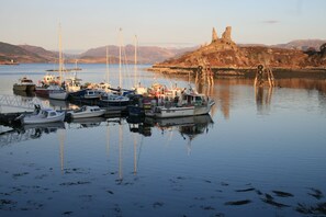 Ein Yachthafen mit vor Anker liegenden Booten, ein Schloss auf einem Hügel im Hintergrund und ruhiges Wasser.
