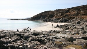 Una spiaggia rocciosa con persone e cielo sereno.