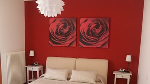 Quarto com uma cama grande, duas mesas de cabeceira, uma luminária pendente branca e duas pinturas abstratas vermelhas na parede.